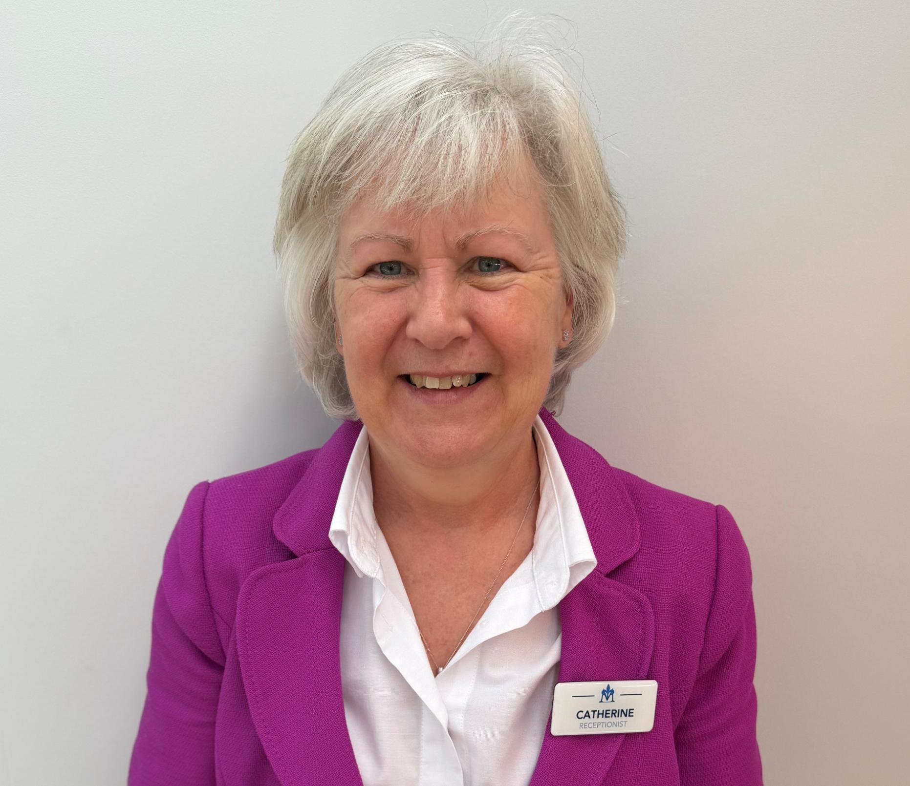 smiling woman with grey hair wearing white shirt and pink blazer
