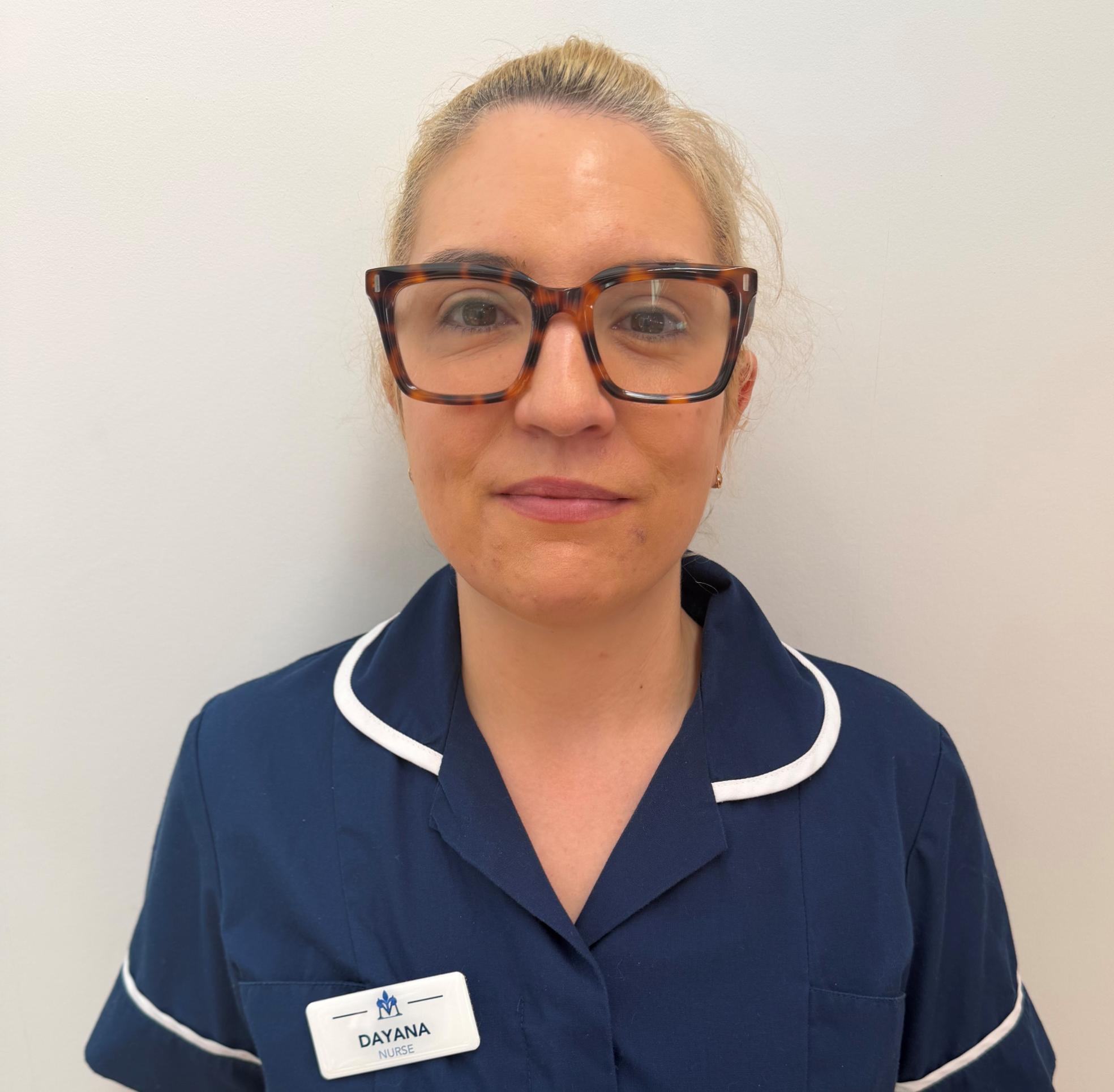 Woman with thick-framed glasses wearing dark blue nurse uniform