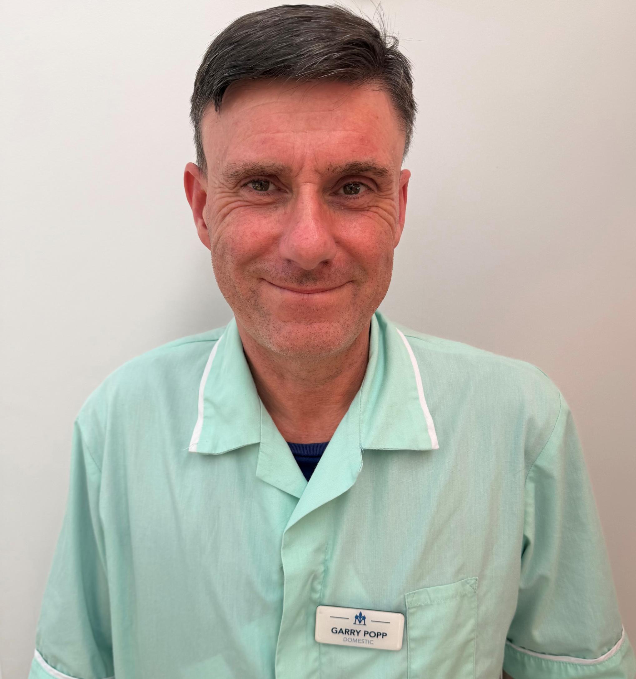 Man smiling in turquoise care home uniform
