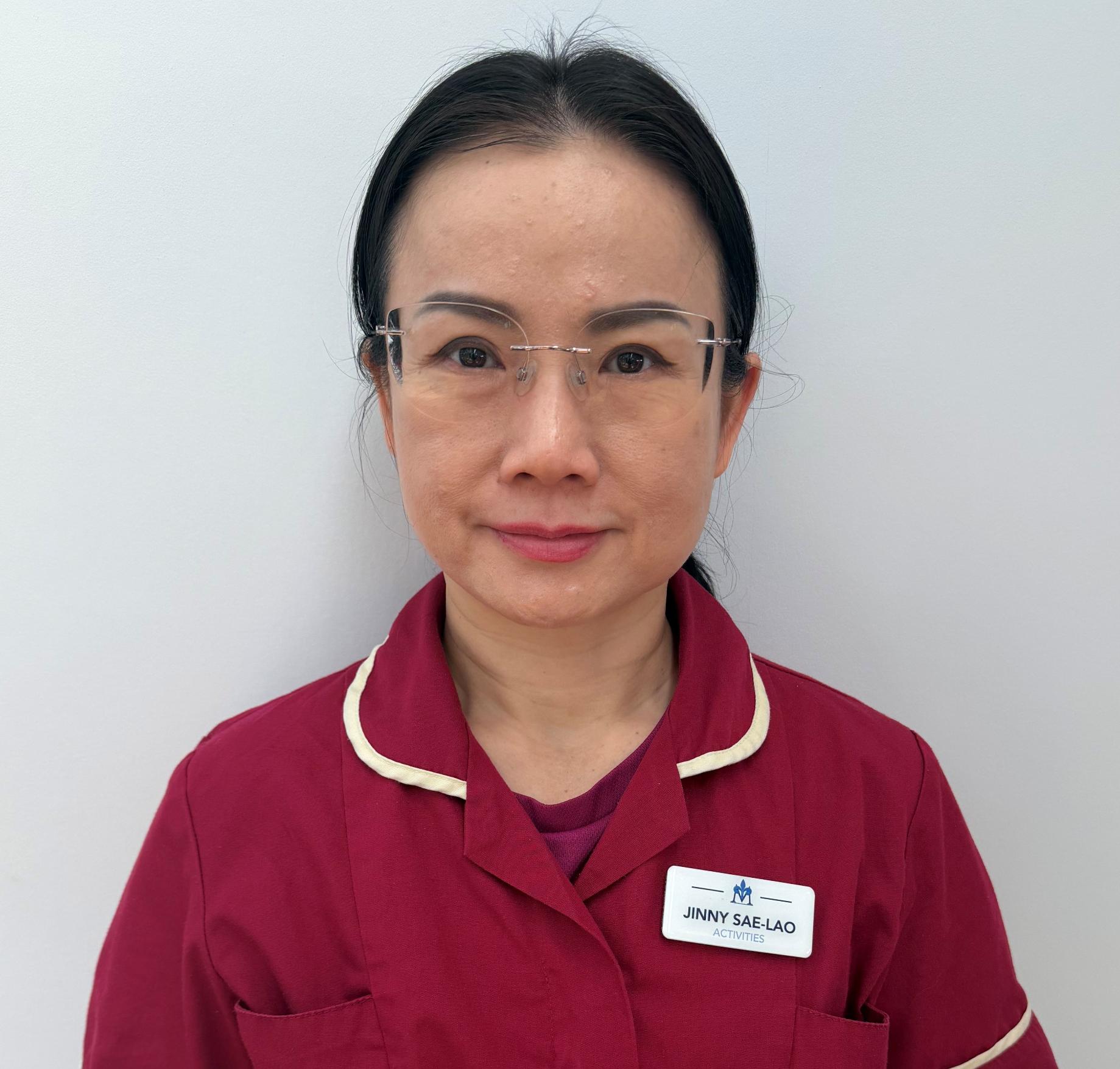woman with glasses smiling in maroon nurses uniform