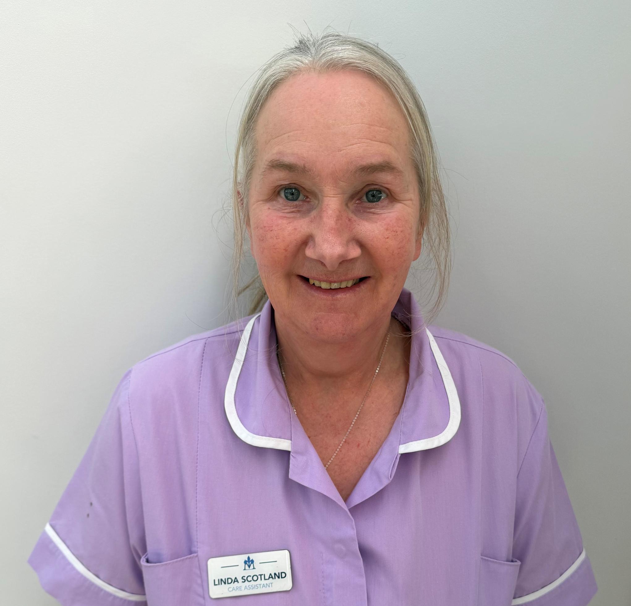 Woman with grey hair smiling in lavender nurses uniform