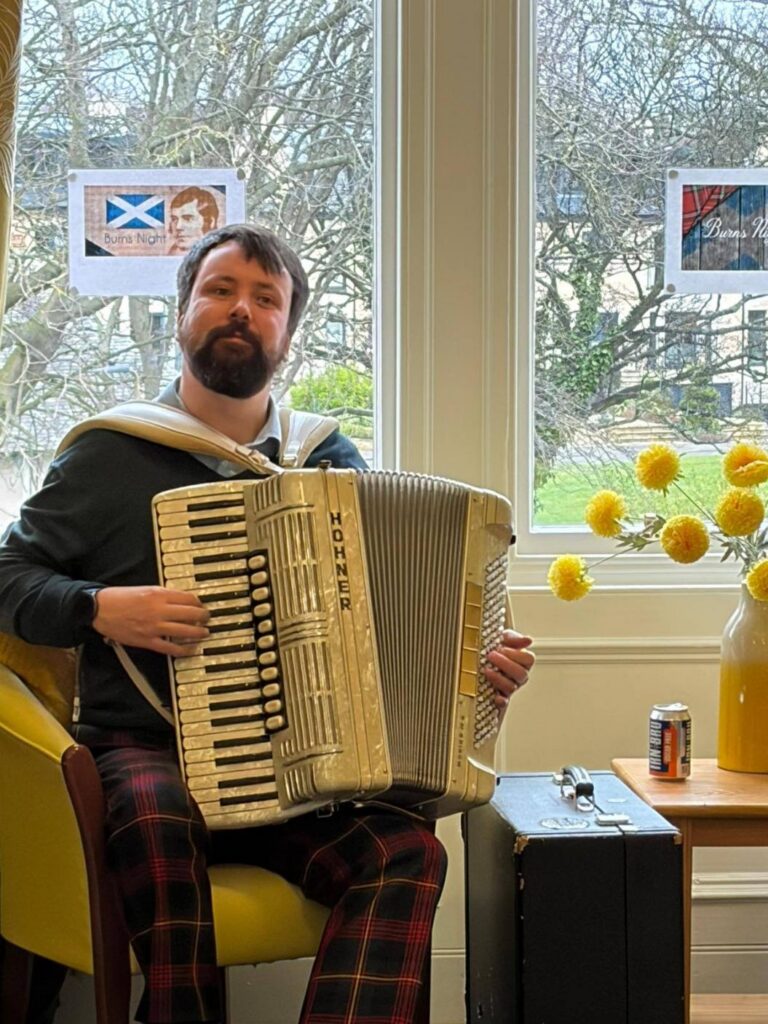man with beard sitting and playing an accordion
