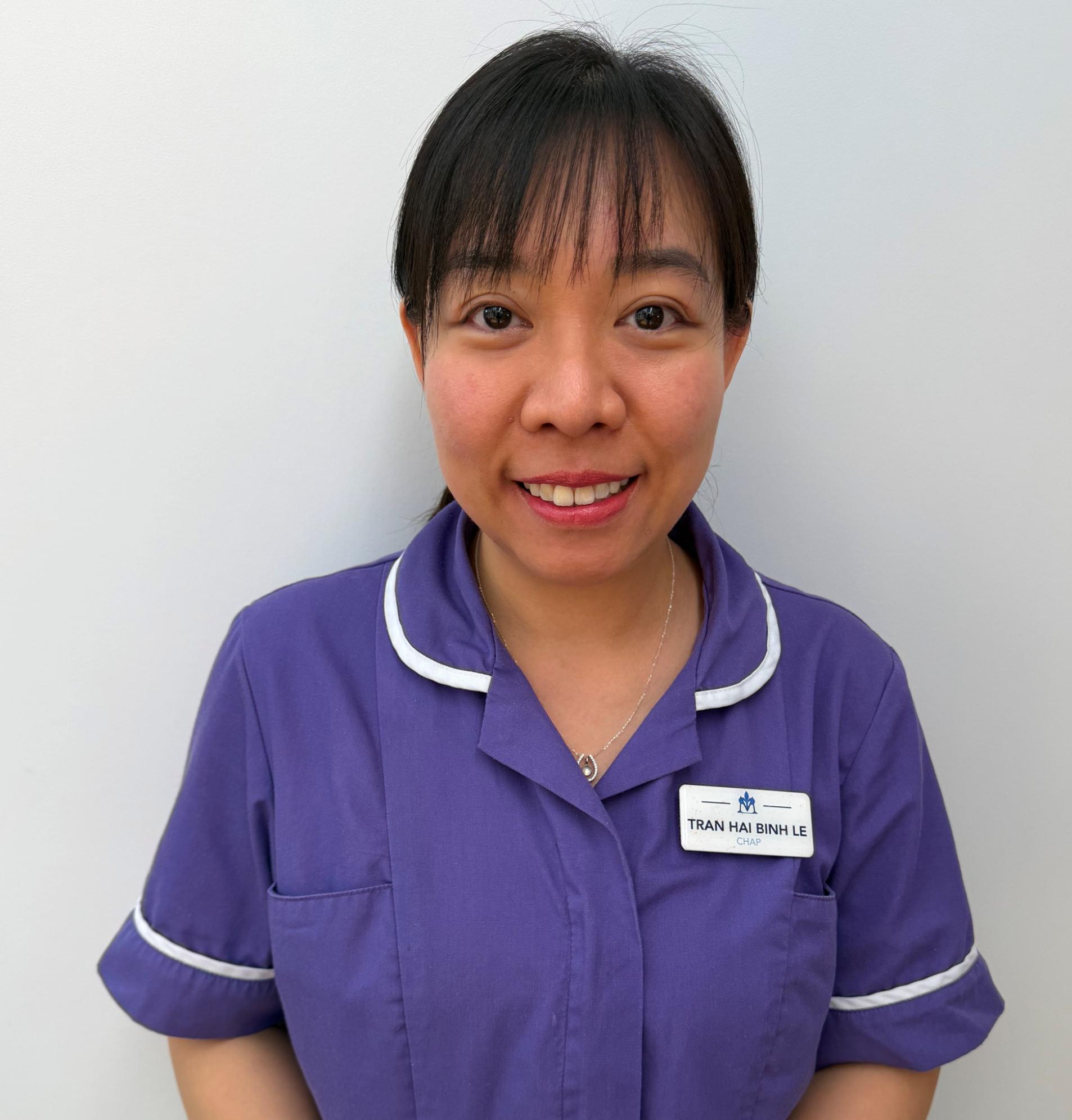care home advanced practitioner smiling with dark hair wearing a purple nurse uniform