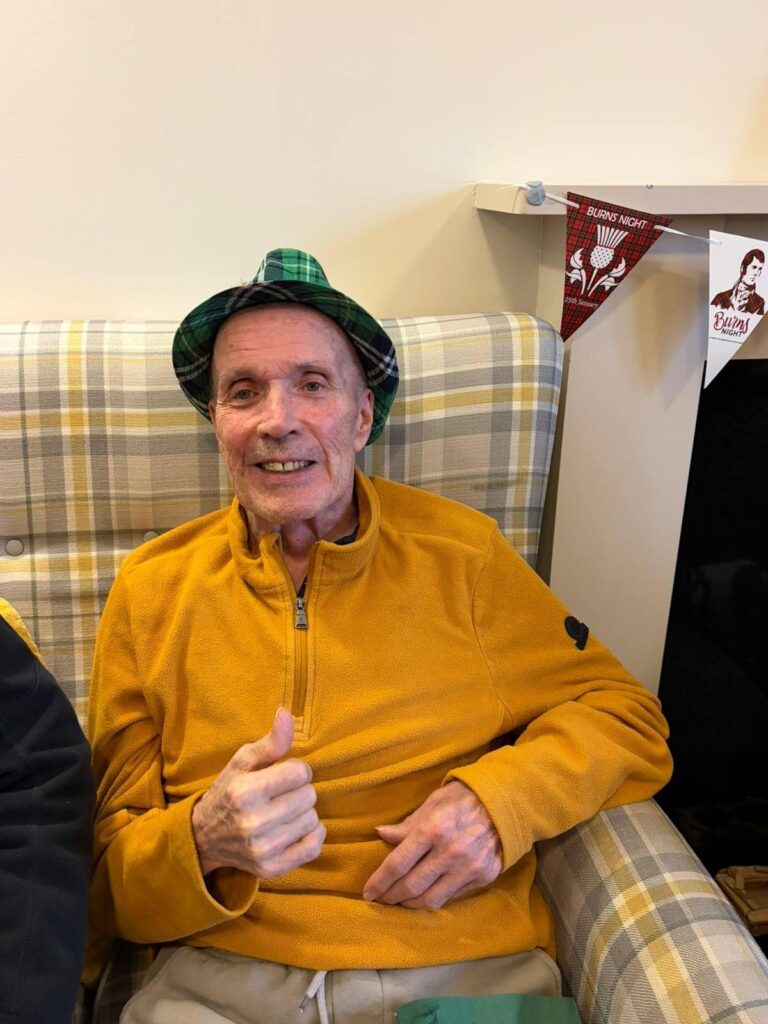 elderly resident dancing in a chair wearing a tartan hat