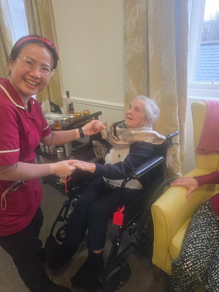 nurse in pink uniform dancing with elderly resident smiling in a wheelchair
