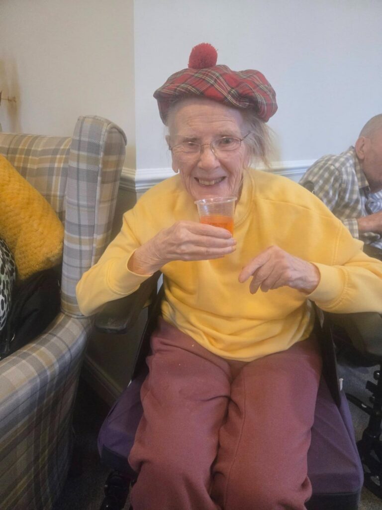elderly woman drinking a cup of irn bru wearing a scottish hat